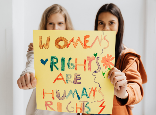 Two girls hold a hand-painted sign that reads \"Women's rights are human rights\"